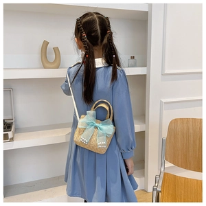 Detail of handmade straw bag with light blue bow and pearl accents on a girl