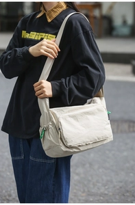 Detail view of a cream nylon messenger bag featuring a wide strap and green zipper pull details
