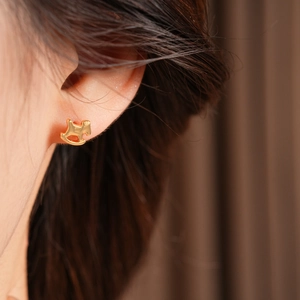 Détail d'une boucle d'oreille cheval à bascule plaquée or portée sur le lobe sur fond flou