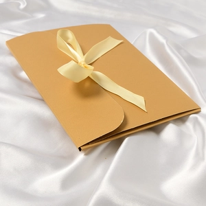 Golden envelope gift box with cream ribbon bow on white silk fabric background