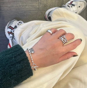 Detail of silver heart charm bracelet and layered rings worn with casual knitwear