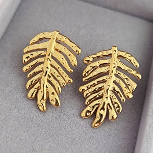 Leaf-shaped brass gold earrings with textured hammer finish on grey velvet tray