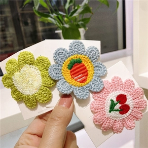 Close-up of handmade crochet flower hair clips featuring pineapple, carrot and cherry motifs