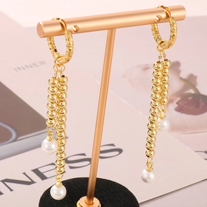 Detail of long gold tassel earrings with white pearls hanging on a display stand