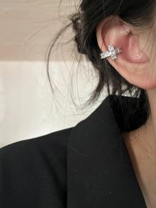 Detailed close-up of a silver cross ear cuff with white zircons on a model's ear