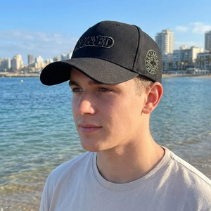 Black cotton baseball cap with gold embroidery worn by a model at the beach