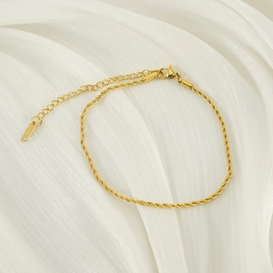Detailed shot of 2mm gold twisted chain anklet with lobster clasp on white fabric