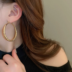 Close-up of a large gold textured hoop earring with a stylish woven metallic surface