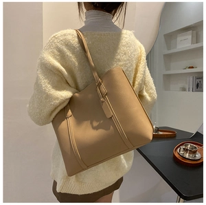 Detail view of large beige leather tote bag with tag showing capacity on model's shoulder