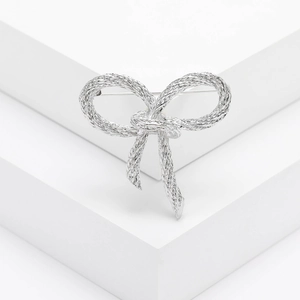 Silver bow brooch with textured metallic finish on a white minimalist display