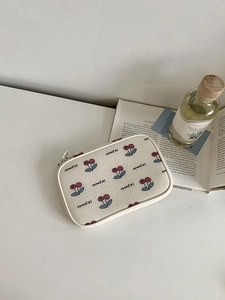 Close-up of a small cream canvas pouch with red cherry patterns and zipper closure