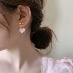 Detailed close-up of a pink heart-shaped drop earring worn by a model on a soft background