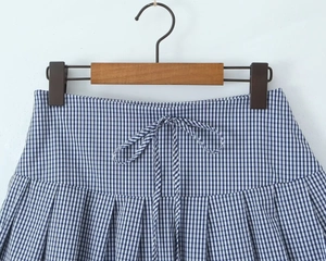 Detail of blue and white plaid mini skirt with waist tie and pleated hem texture