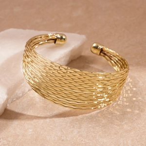 Close-up of golden multi-layer wavy textured open cuff bracelet on stone stand