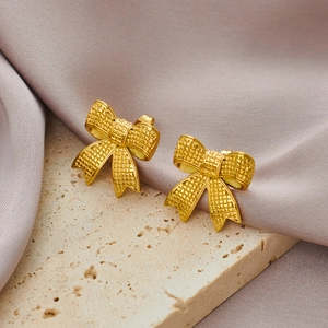 Detail of gold bow earrings featuring a textured woven pattern on a silk background