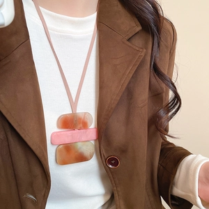 Detail of acrylic block pendant necklace styled with elegant brown vintage blazer