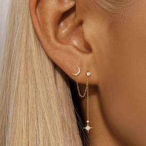 Detail of gold double piercing chain earrings with crescent moon and starburst dangles