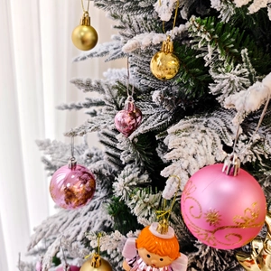 Détail de boules de Noël roses et dorées et pendentif ange sur une branche enneigée