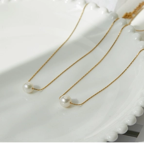Detail shot of a minimalist gold pearl necklace on a white decorative ceramic plate
