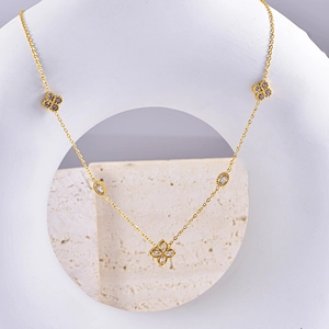 Detailed macro of gold clover necklace with zircon inlays on minimalist white display