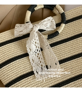 Detailed close-up of straw tote bag with horizontal stripes and white lace bow handle