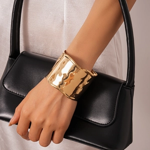 Detailed view of wide gold metallic bracelet with hammer texture on model hand