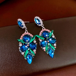Close-up of teardrop earrings with blue gemstone, green petals, and pink accents