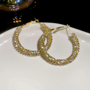 Macro detail of luxury gold hoop earrings with pavé crystals on a ceramic tray