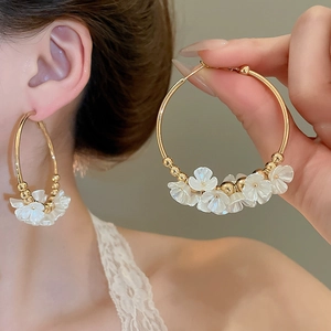 Detail view of golden hoop earring featuring 3D white acrylic flowers with pearly luster