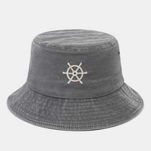 Detail of white embroidered ship helm logo on washed cotton grey bucket hat surface