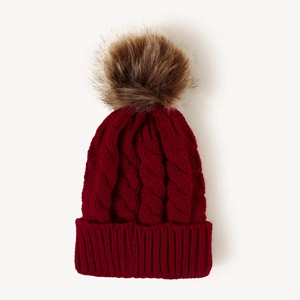 Detail showing red cable knit beanie texture with a fluffy brown faux fur pom pom