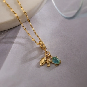 Goldene Halskette Detail mit Blatt, Fisch und grünem Edelstein auf weißem Teller