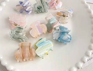 Close-up of colorful marble acrylic mini hair claws on a decorative white ceramic tray