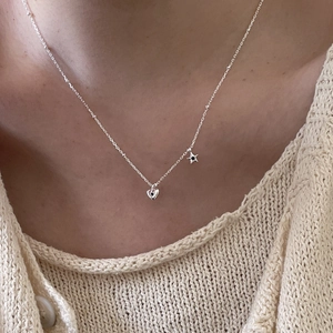 Detail of silver chain necklace with heart and star pendants on a knitted sweater
