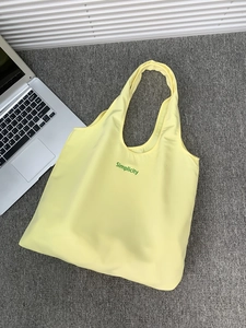 Close-up of bright yellow canvas tote bag with green Simplicity lettering and laptop