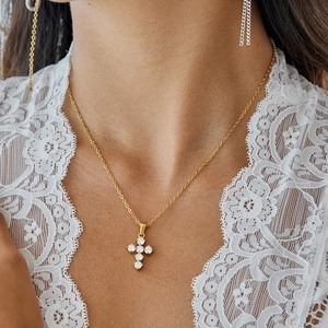 Dettaglio della collana con pendente a croce dorata e pietre di zirconi su modella