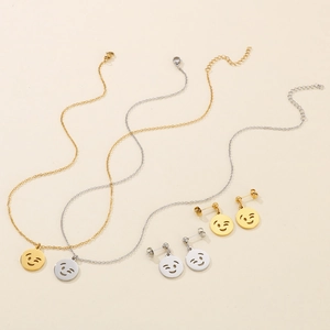 Detail of gold and silver smiley face necklace and earrings set on beige background