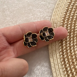 Macro detail of camellia flower stud earrings with black enamel and gold edging
