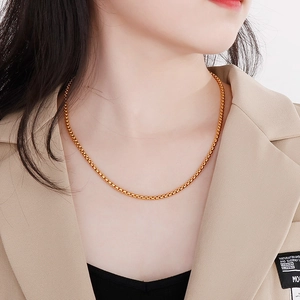 Close-up of golden stainless steel box chain necklace worn by a model in a beige suit