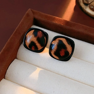 Vue macro de boucles d'oreilles carrées léopard avec bordure noire dans leur écrin