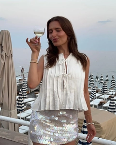 Detail of white pleated sleeveless top with tie-neck and silver sequin mini skirt