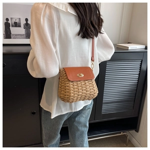 Detailed view of woven straw shoulder bag with brown leather flap and gold twist lock