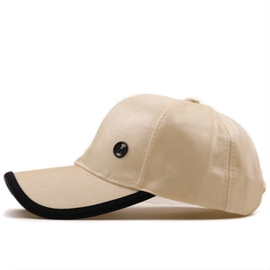 Close-up of beige satin baseball cap with black M-letter badge and contrast brim detail