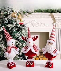 Three plush Christmas figurines including Santa, elk, and snowman displayed by a cozy fireplace