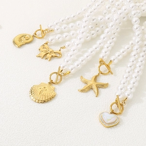 Detailed view of pearl necklaces with gold charms like shells and hearts on white surface