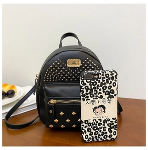 Detail view of mini black PU leather backpack with gold rivets on a wooden table