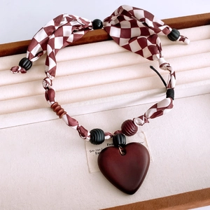 Close-up of heart-shaped wooden pendant on checkered fabric necklace with beads