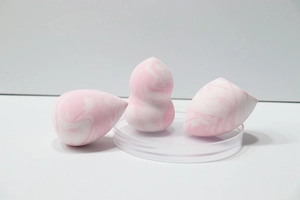 Macro view of pink marble makeup sponge set on glass dish with three unique shapes