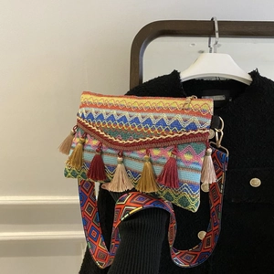 Detail of bohemian woven crossbody bag featuring colorful tassels and patterned wide strap