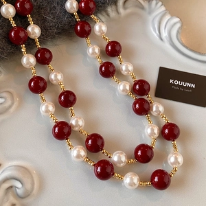 Elegante collana di perle rosse Ankara e bianche con maglie dorate vintage su sfondo grigio